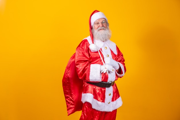 Настоящий Санта-Клаус с красным фоном, в очках, перчатках и шляпе смотрит сбоку.