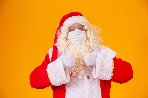 Real santa claus on yellow background, wearing protective mask against the covid19. christmas with social distance. covid-19