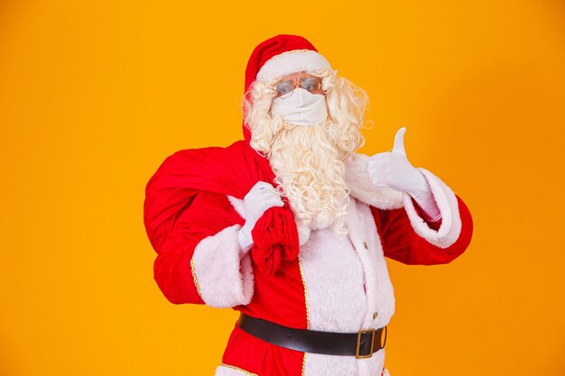 Real Santa Claus on yellow background, wearing protective mask against the covid19. Christmas with social distance. Covid-19