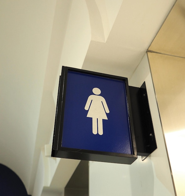 Реальный знак туалета или вкладка направления туалета и висит на стене и синий цвет и белый значок.
