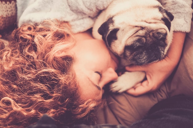 Foto vero vero amore tra la mezza età bella donna caucasica che dorme e protegge, i suoi migliori amici cane carlino. amicizia e relazione a casa nel concetto di vita