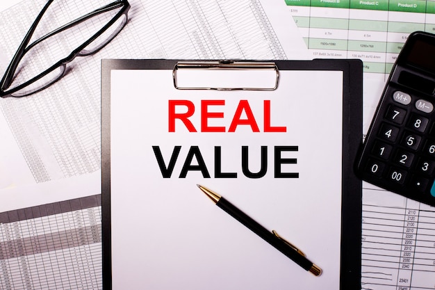 REAL VALUE is written on a white sheet of paper, near the glasses and the calculator.