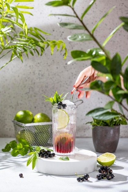 Photo real woman preparing black currant mojito cocktail in highball glass elegant glass filled with cocktail or mocktails surrounded by ingredients on gray table surface ready for drinking