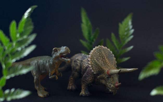 Foto figure realistiche dei dinosauri tirannosauro e triceratopo sotto succose foglie verdi