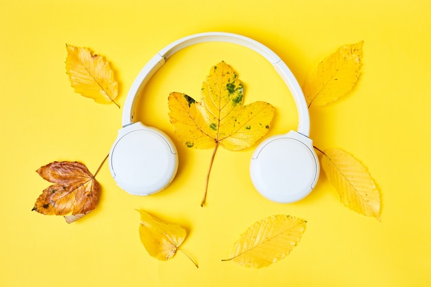 노란색 배경 가을 또는 팟캐스트 재생 목록에 있는 현실적인 나뭇잎과 흰색 헤드폰