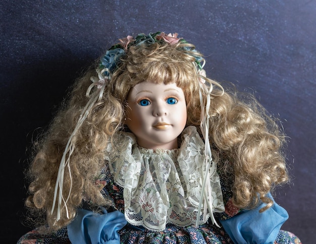 realistic vintage porcelain doll toy with blue eyes dressed in a blue dress and has a blond hair