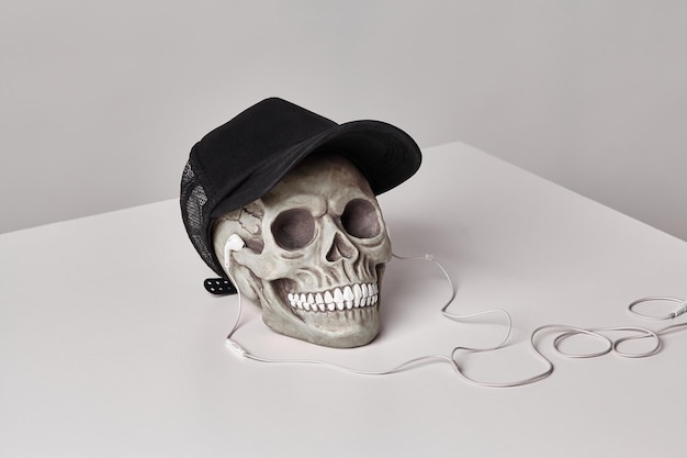 Realistisch model van een menselijke schedel met tanden in een zwarte baseballcap en koptelefoon op een lichte tafel witte achtergrond medische wetenschap of Halloween horror concept close-up shot