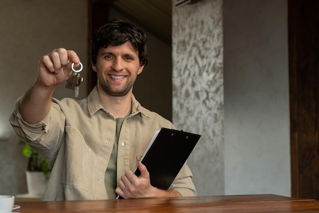 A realtor or real estate agent shows the key to the house he sold Portrait of a man standing in the living room holding a folder and a key smiling looking at the camera