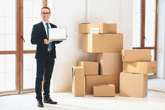 Realtor in suit holding laptop with white screen.