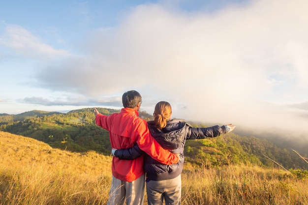 Rear of happy couple love stand on top mountain looking view with mist and cloud at Doi Langka Luang, Chiang Rai province. soft focus.