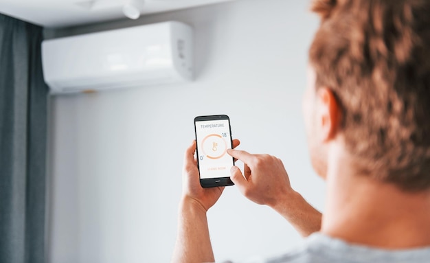 Rear view of adult man that is indoors controlling smart home technology