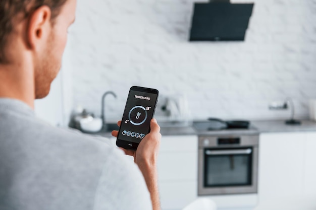 Rear view of adult man that is indoors controlling smart home technology