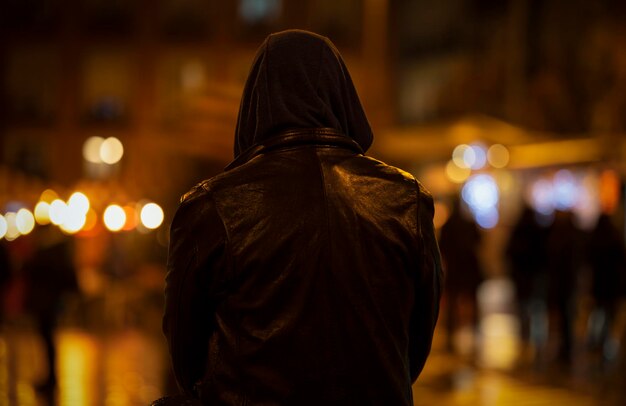 Rear view of adult man with hood on street at night