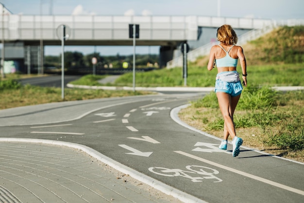 Rear view of an adult woman running on riverside city promenade and listening music.