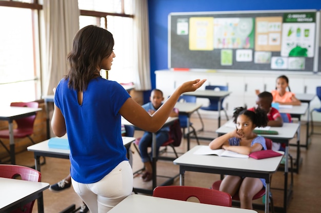 Rear view of african american female teacher teaching students in the class at elementary school