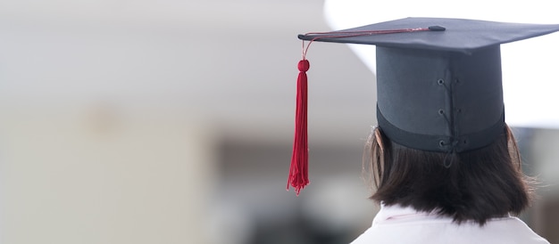 背面図卒業帽をかぶったアジアの女子校生の卒業生は、巻かれた証明書を持っています。卒業祝いのコンセプトストックフォト