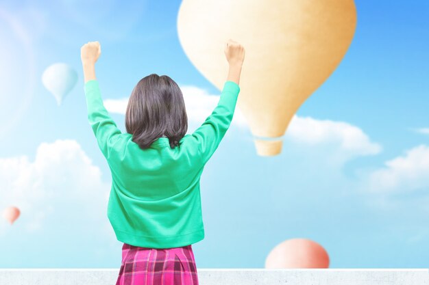 Vista posteriore della bambina asiatica che guarda una mongolfiera colorata che vola con lo sfondo del cielo blu