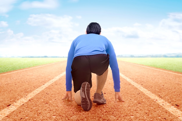 Rear view of Asian runner man ready to run on the running track