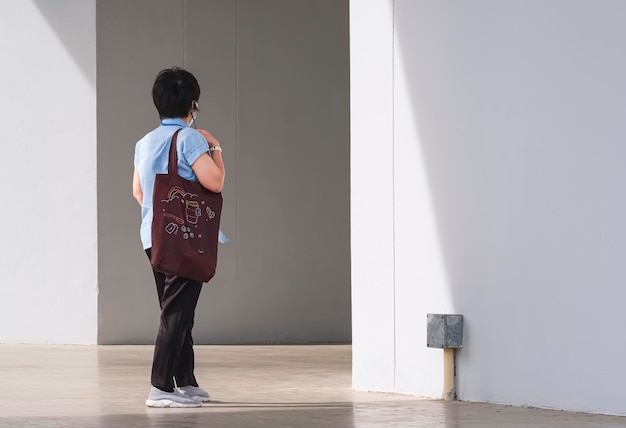 Rear view of Asian woman carrying brown reusable eco friendly tote bag is walking into supermarket