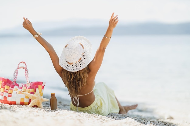 Rear view on an attractive woman in bikini, with summer hat, is having fun while enjoying a summer vacation on the beach.