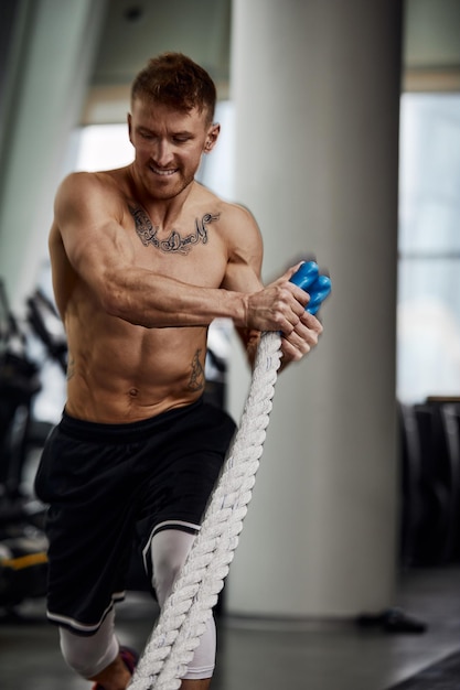 Rear view of Attractive young fit and toned sportswoman working out with battle ropes. Motion blur