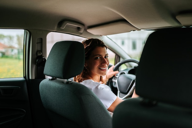 Rear view of attractive young woman in casual wear looking over her shoulder while driving a car.