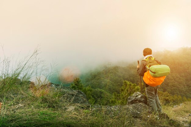 Photo rear view of backpack man standing on mountain peak during foggy weather