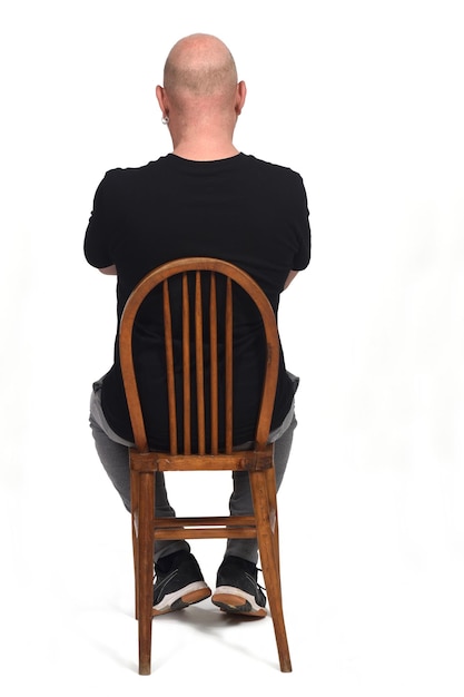 Photo rear view of a bald man siiting on a chair with sportiswear on white background, arms crossed