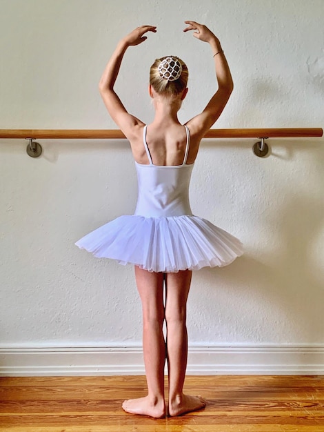 Photo rear view of ballet dancer with arms raised standing against wall