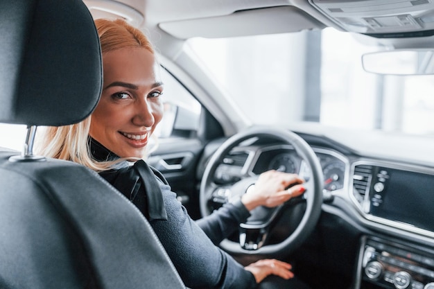 Rear view of beautiful blonde in elegant clothes that sitting inside of modern car