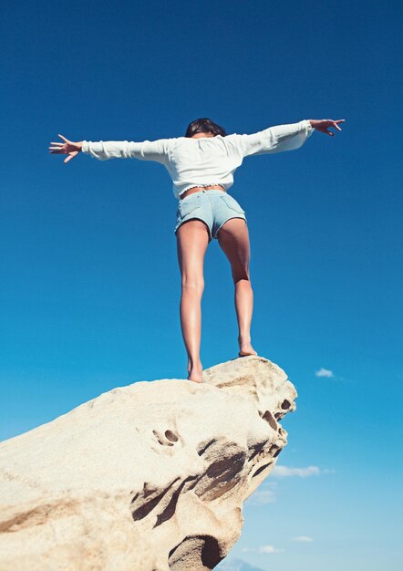 Photo rear view of a beautiful brunette young girl with raised hands looking at ocean freedom concept holiday on beach with clear sky background