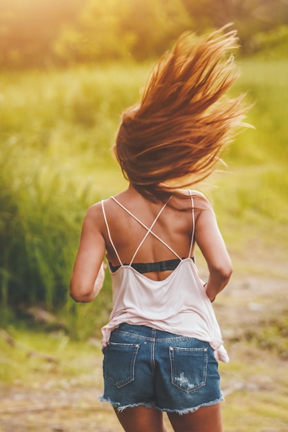 Rear view of a beautiful young woman enjoying summer, relaxing and running in the nature fringed with lush scenery.