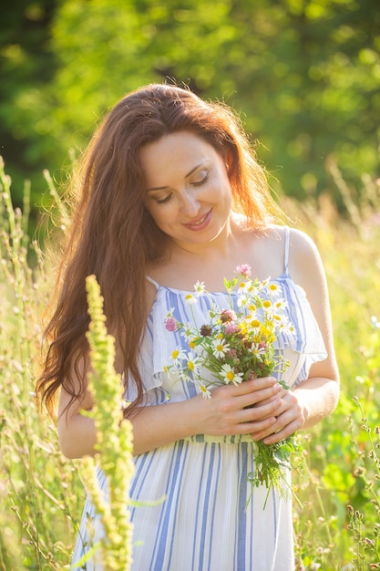 Rear view of beautiful young woman walking among wildflowers on sunny summer day. Joy of communicating with summer nature