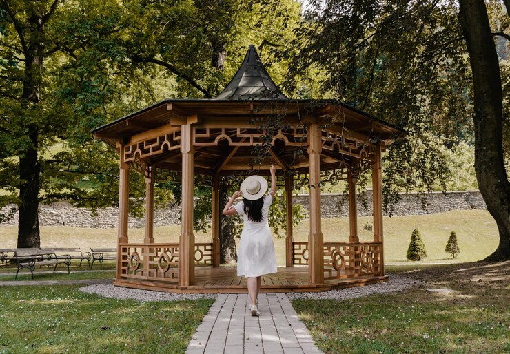 Photo rear view of beautiful young woman wearing white dress standing under wooden pavilion in park