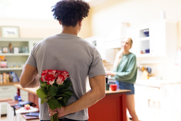 Rear view of biracial young man hiding red roses behind back while talking with wife at home. Unaltered, couple, love, togetherness, surprise, romance, flower, wedding, anniversary.