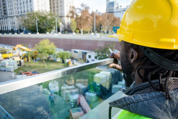 上から建設現場を監督する安全ヘルメットをかぶった黒人男性エンジニアの背面図