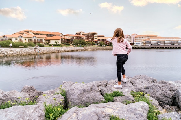 Rear view of a blonde Caucasian girl throwing stones into a village lake