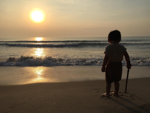 rear view of boy at beach against sky during sunset