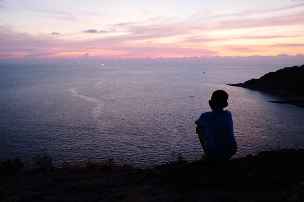 Rear view of boy looking at sea against sunset sky