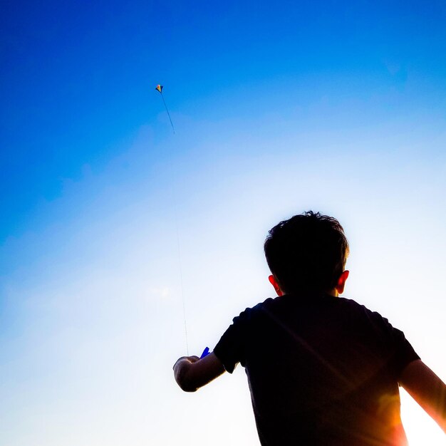 Rear view of boy playing against blue sky