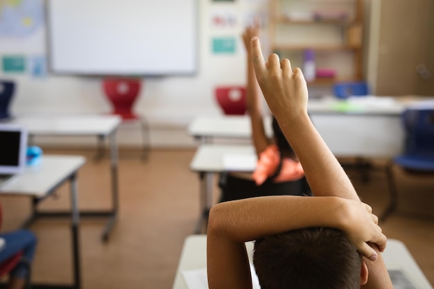 Foto vista posteriore del ragazzo che alza la mano per la partecipazione alla classe della scuola elementare