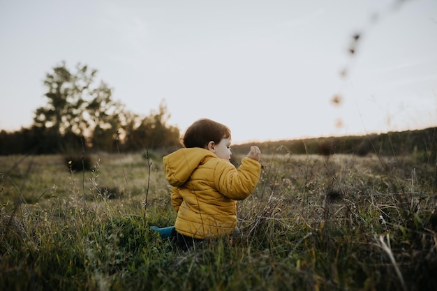 Rear view of boy sitting on grass against sky
