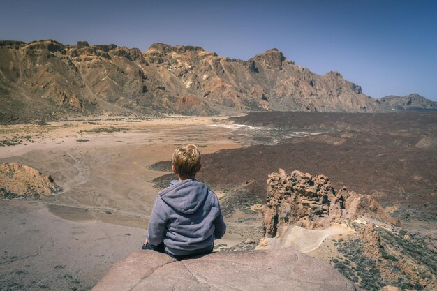 Foto vista posteriore di un ragazzo seduto su una roccia nel deserto