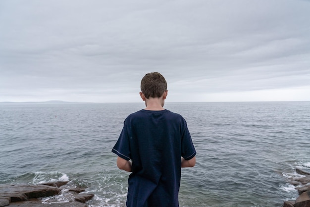 rear view of boy standing at beach against sky