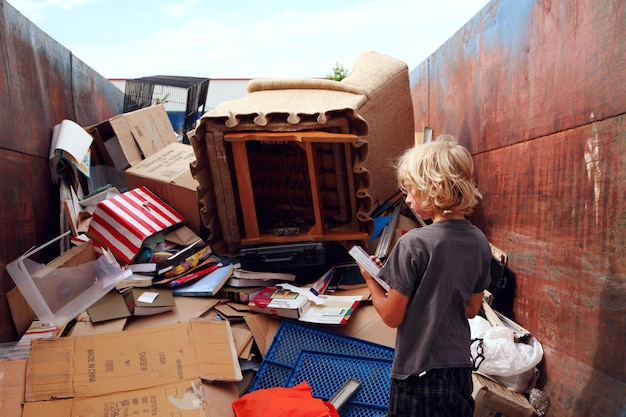 Photo rear view of boy standing by abandoned objects in dumpster