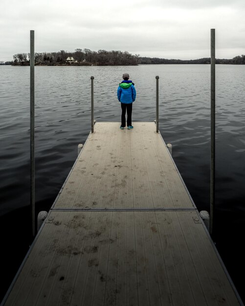 Foto vista posteriore di un ragazzo in piedi sul molo sul lago contro il cielo