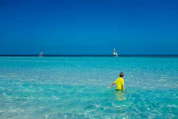 Rear view of boy standing in sea against clear blue sky