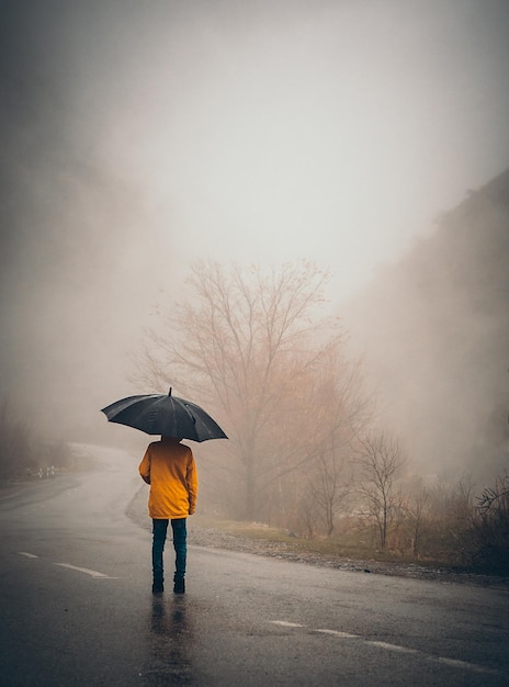 雨季の湿った道路に立っている少年の後ろの景色