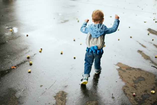 湿った通りで立っている少年の後ろの景色