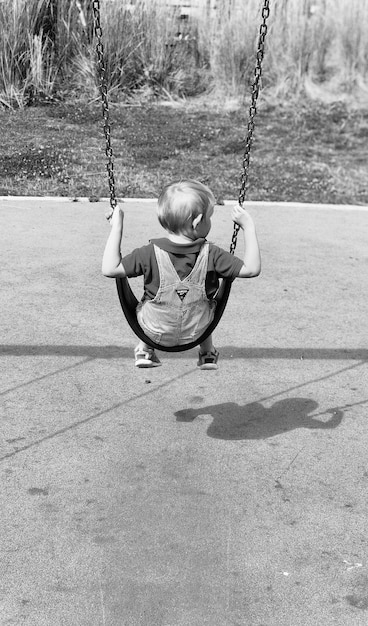 Photo rear view of boy swinging at playground during sunny day